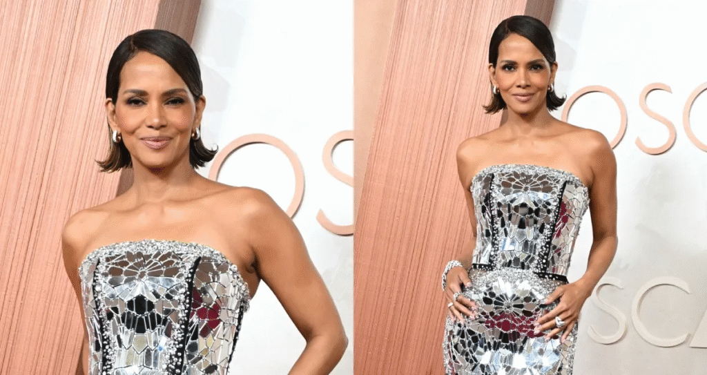 Halle Berry wearing a strapless mirrored silver gown with sleek short hair, posing confidently on the red carpet at a glamorous event